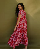 Woman wearing long flowy tiered short sleeve dress with pink floral on red ground.