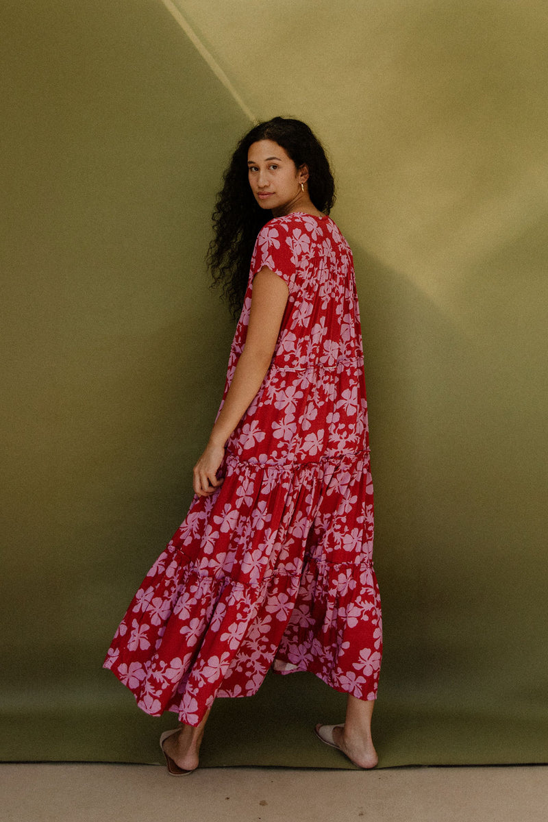 Woman wearing long flowy tiered short sleeve dress with pink floral on red ground.