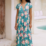 woman with brown hair wearing a tiered maxi dress in teal with large cream colored orchids.