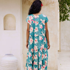 woman with brown hair wearing a tiered maxi dress in teal with large cream colored orchids.