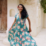 woman with brown hair wearing a tiered maxi dress in teal with large cream colored orchids.