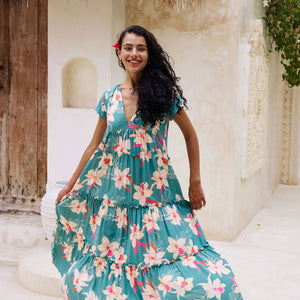 woman with brown hair wearing a tiered maxi dress in teal with large cream colored orchids.