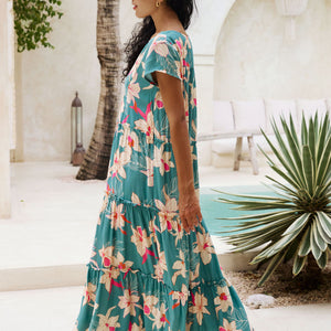 woman with brown hair wearing a tiered maxi dress in teal with large cream colored orchids.