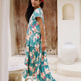 woman with brown hair wearing a tiered maxi dress in teal with large cream colored orchids.