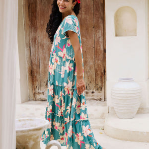 woman with brown hair wearing a tiered maxi dress in teal with large cream colored orchids.