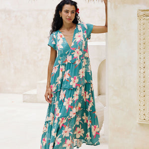 woman with brown hair wearing a tiered maxi dress in teal with large cream colored orchids.