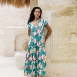 woman with brown hair wearing a tiered maxi dress in teal with large cream colored orchids.