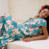 woman with brown hair wearing a tiered maxi dress in teal with large cream colored orchids.