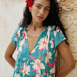 woman with brown hair wearing a tiered maxi dress in teal with large cream colored orchids.