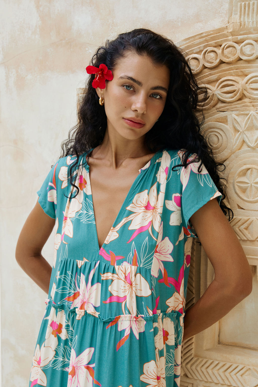 woman with brown hair wearing a tiered maxi dress in teal with large cream colored orchids.