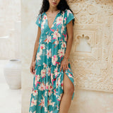woman with brown hair wearing a tiered maxi dress in teal with large cream colored orchids.