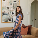 woman with black hair wearing a tiered maxi dress with v neckline in a navy and pink hibiscus print. 