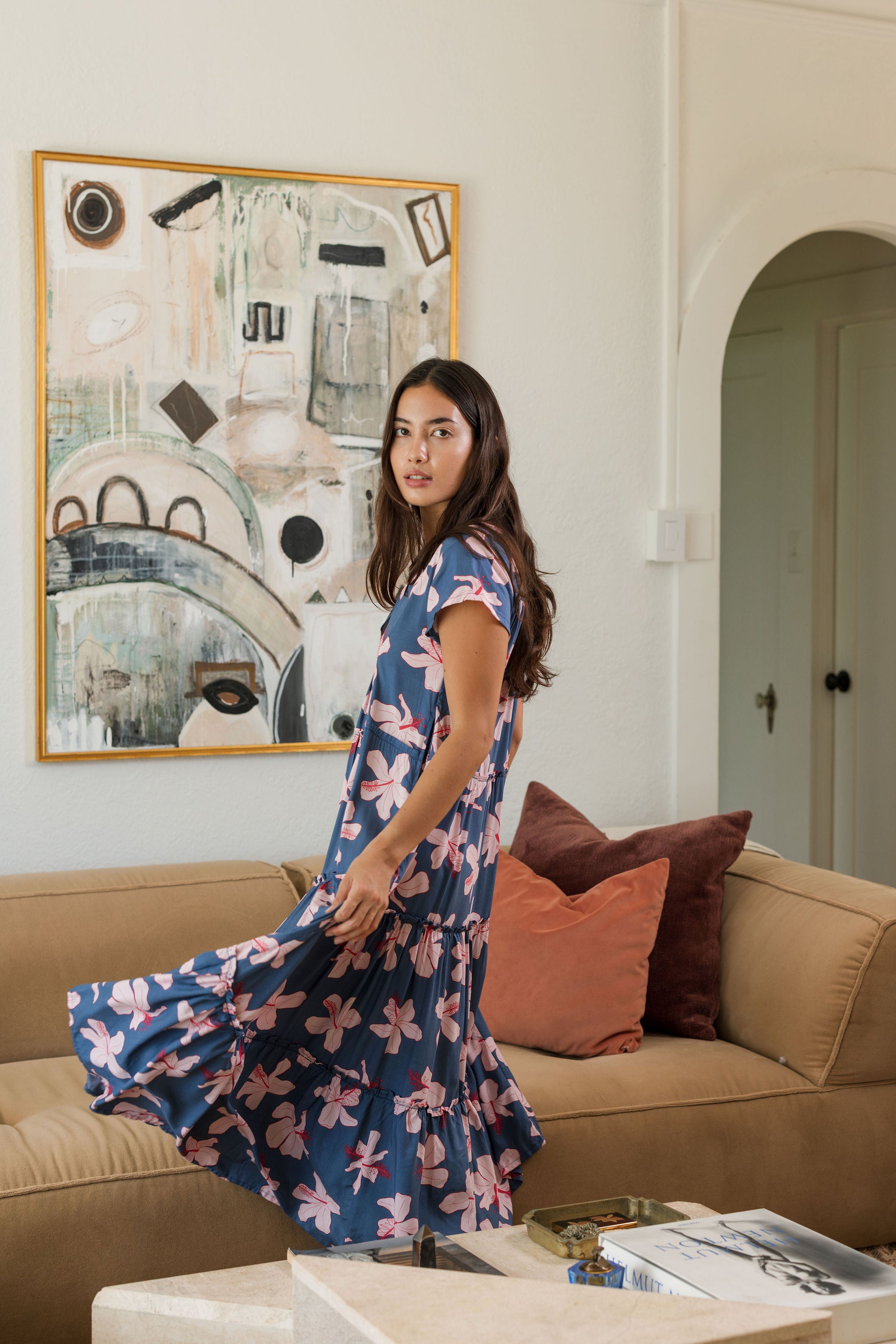 woman with black hair wearing a tiered maxi dress with v neckline in a navy and pink hibiscus print. 