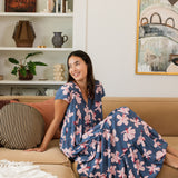 woman with black hair wearing a tiered maxi dress with v neckline in a navy and pink hibiscus print. 