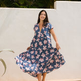 woman with black hair wearing a tiered maxi dress with v neckline in a navy and pink hibiscus print. 