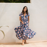 woman with black hair wearing a tiered maxi dress with v neckline in a navy and pink hibiscus print. 