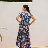 woman with black hair wearing a tiered maxi dress with v neckline in a navy and pink hibiscus print. 
