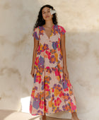 Woman in long flowy tiered dress with short sleeves and multi colored floral print with light pink ground.