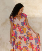 Woman in long flowy tiered dress with short sleeves and multi colored floral print with light pink ground.