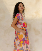 Woman in long flowy tiered dress with short sleeves and multi colored floral print with light pink ground.