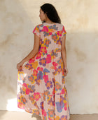 Woman in long flowy tiered dress with short sleeves and multi colored floral print with light pink ground.