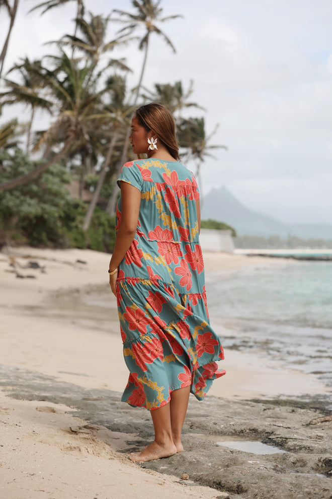woman with brown hair wearing long flowy green maxi dress with orange and yellow lei pua print