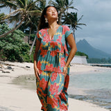 woman with brown hair wearing long flowy green maxi dress with orange and yellow lei pua print