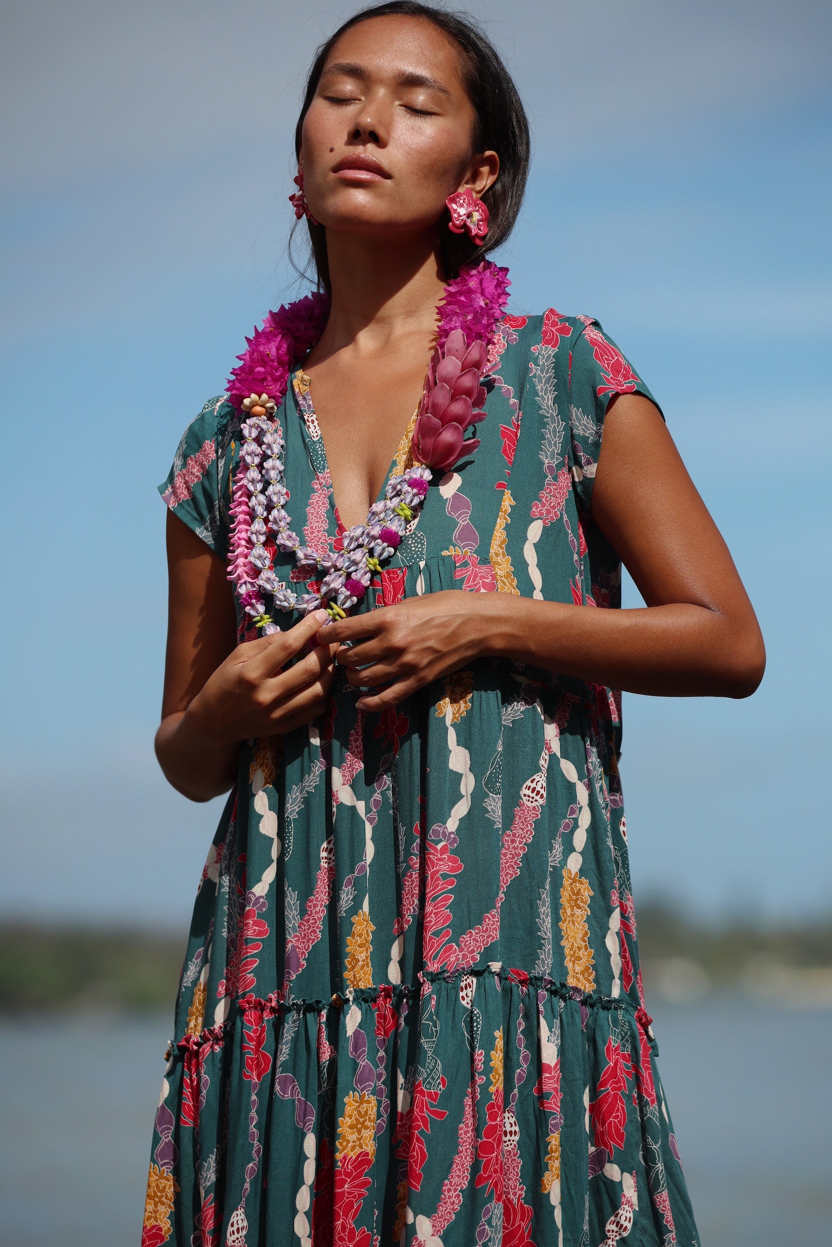woman with brown hair wearing long tiered maxi dress in dark teal with shell lei print