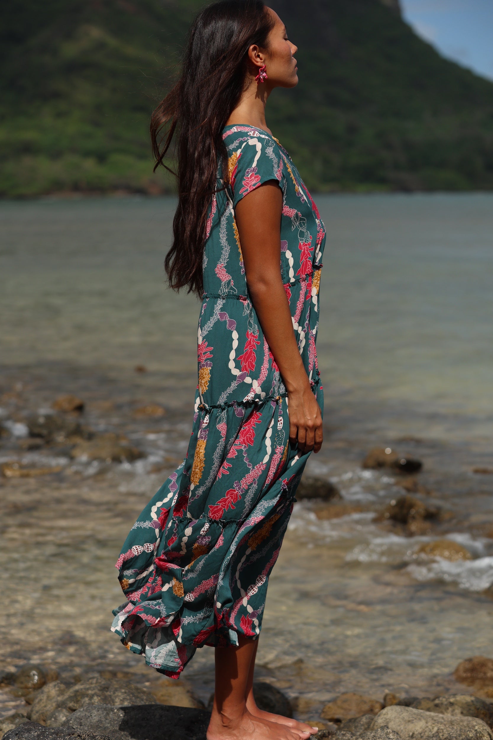 woman with brown hair wearing long tiered maxi dress in dark teal with shell lei print