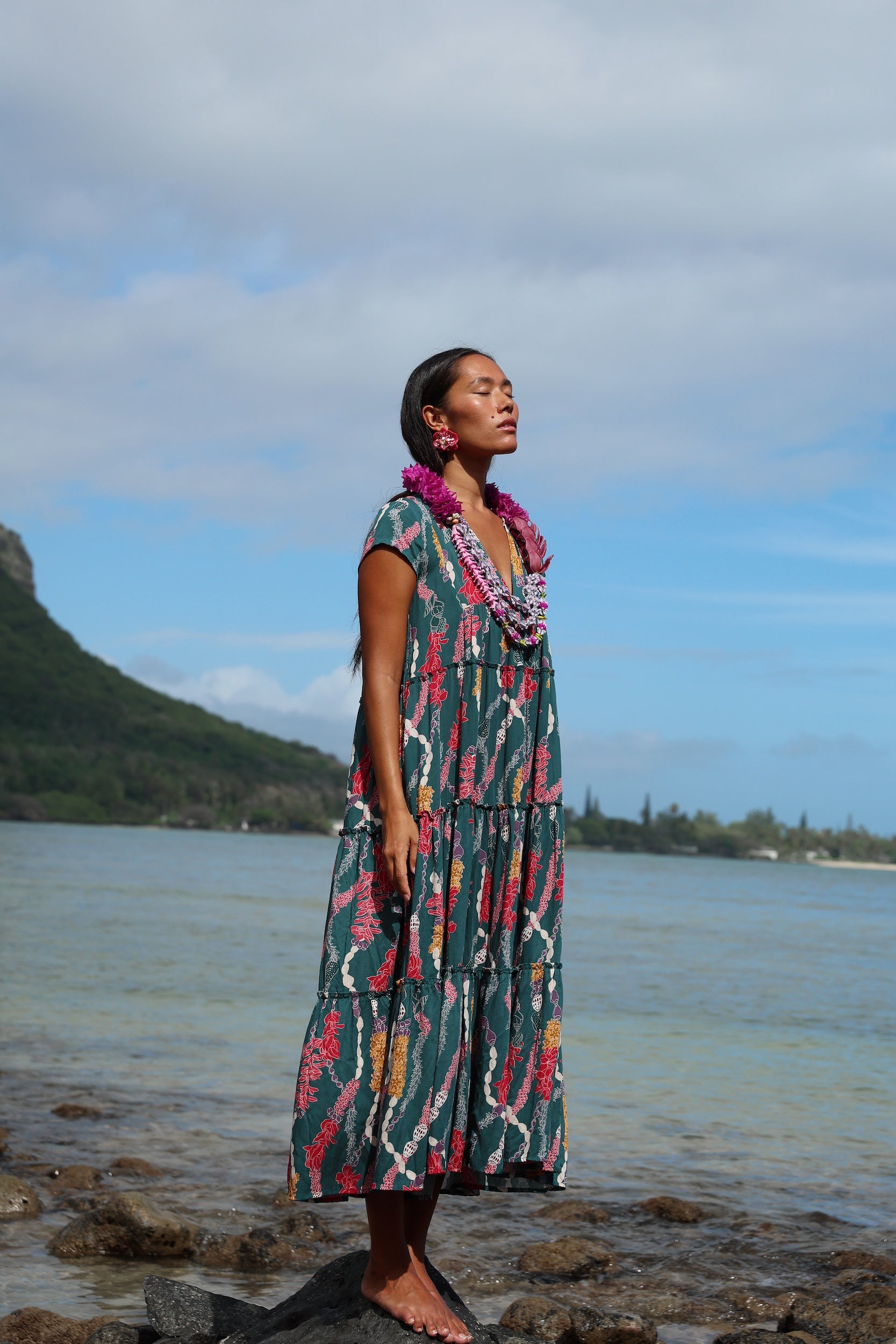 woman with brown hair wearing long tiered maxi dress in dark teal with shell lei print