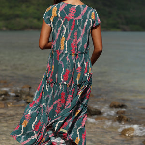 woman with brown hair wearing long tiered maxi dress in dark teal with shell lei print