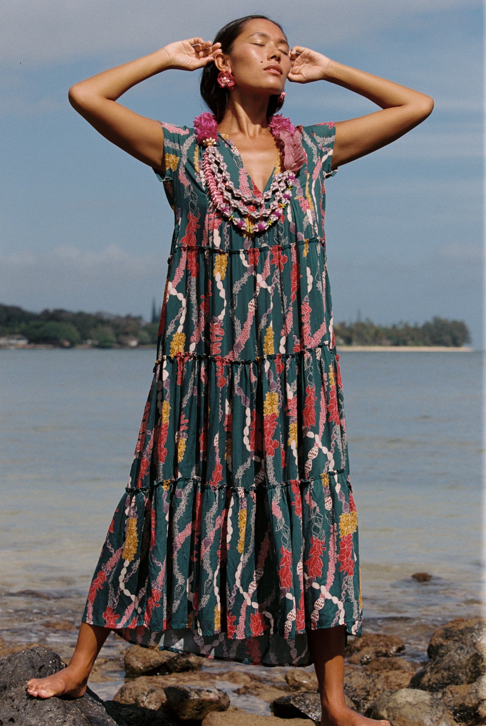 woman with brown hair wearing long tiered maxi dress in dark teal with shell lei print