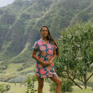 woman with brown hair wearing a navy tailored shirt dress with bright pink hibiscus