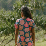 woman with brown hair wearing a navy tailored shirt dress with bright pink hibiscus