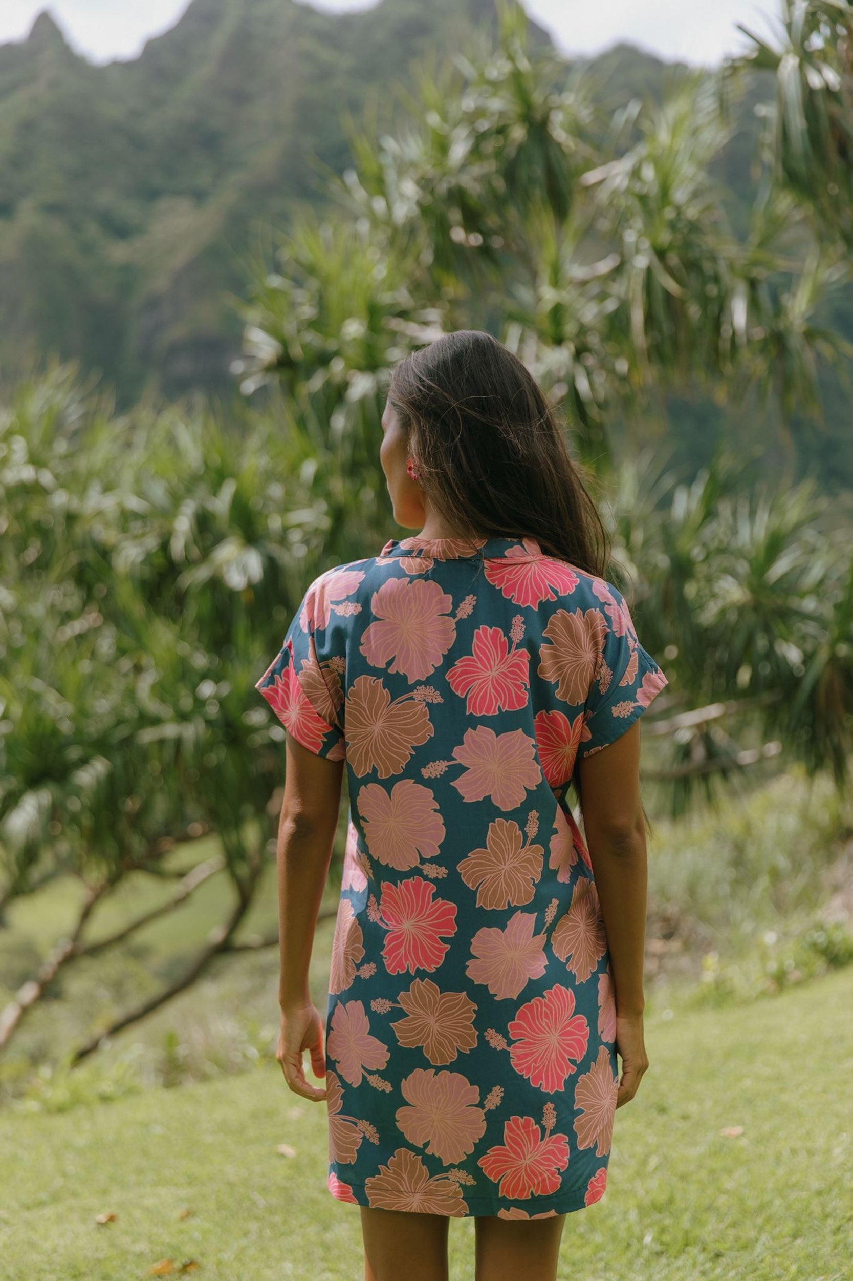 woman with brown hair wearing a navy tailored shirt dress with bright pink hibiscus