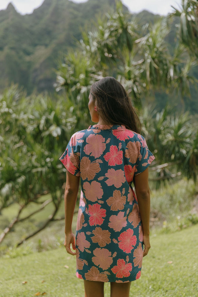 woman with brown hair wearing a navy tailored shirt dress with bright pink hibiscus