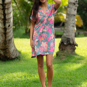 woman with brown hair wearing a teal v neck mini dress with orange and pink foral print