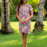 woman with brown hair wearing a teal v neck mini dress with orange and pink foral print