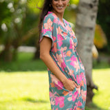 woman with brown hair wearing a teal v neck mini dress with orange and pink foral print