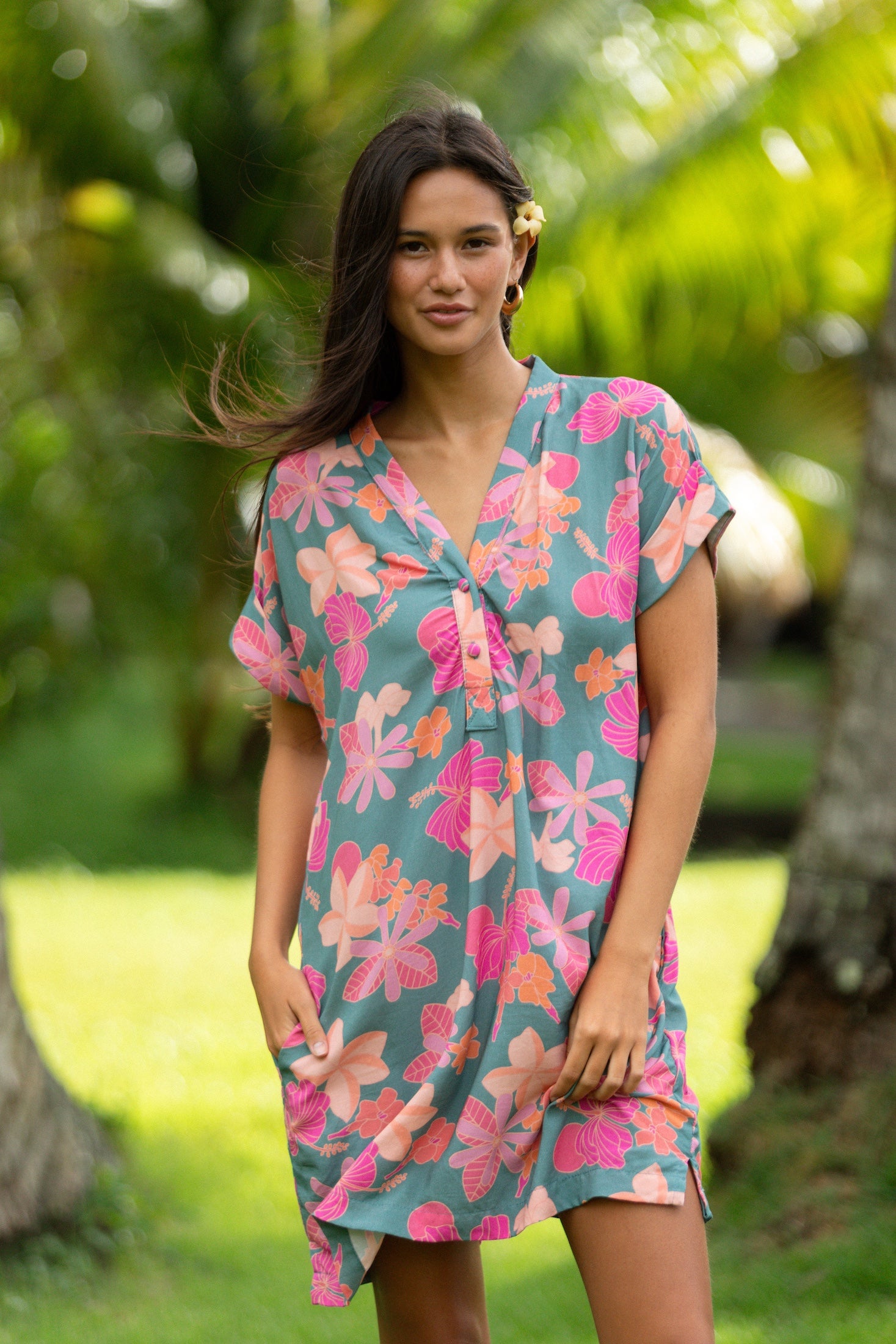 woman with brown hair wearing a teal v neck mini dress with orange and pink foral print