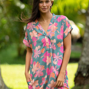 woman with brown hair wearing a teal v neck mini dress with orange and pink foral print
