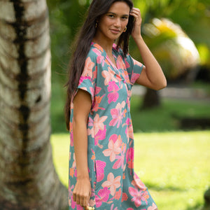 woman with brown hair wearing a teal v neck mini dress with orange and pink foral print