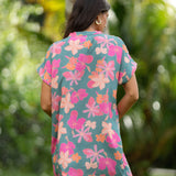 woman with brown hair wearing a teal v neck mini dress with orange and pink foral print