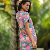 woman with brown hair wearing a teal v neck mini dress with orange and pink foral print