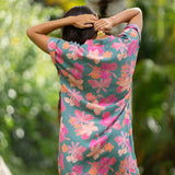 woman with brown hair wearing a teal v neck mini dress with orange and pink foral print