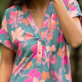  woman with brown hair wearing a teal v neck mini dress with orange and pink foral print