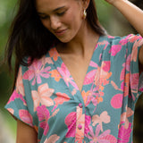 woman with brown hair wearing a teal v neck mini dress with orange and pink foral print