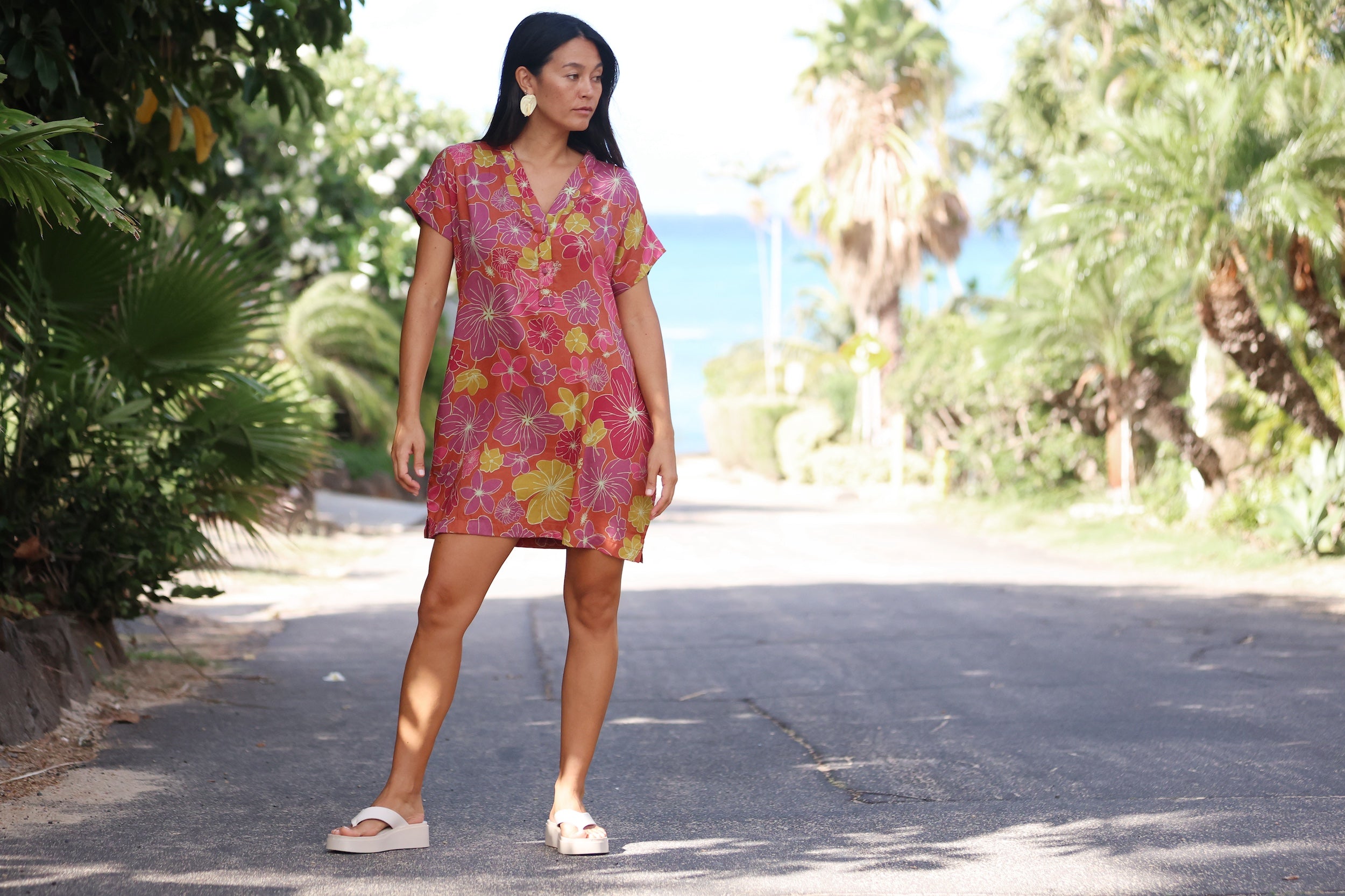 woman with brown hair wearing terracotta colored v neck shirt dress with large purple and yellow flowers