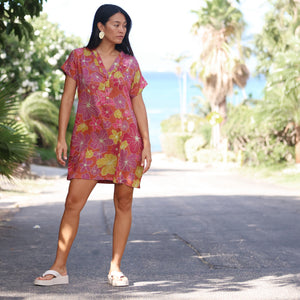 woman with brown hair wearing terracotta colored v neck shirt dress with large purple and yellow flowers