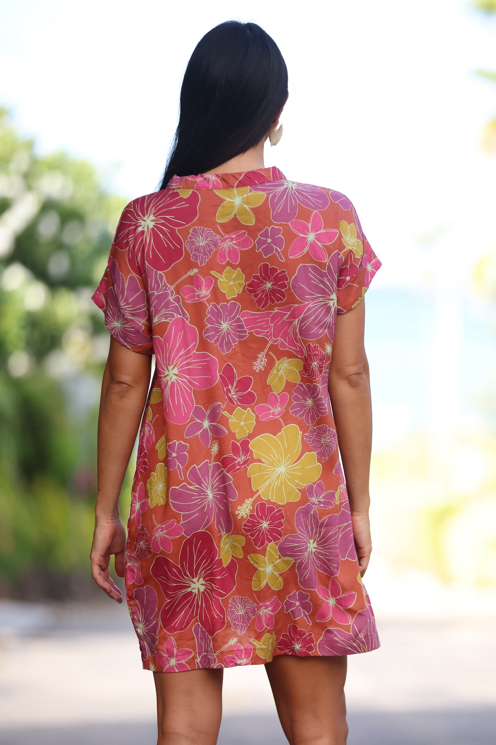 woman with brown hair wearing terracotta colored v neck shirt dress with large purple and yellow flowers